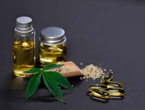 Verschiedene CBD Produkte wie Öl, Kapseln und Salz auf einem dunkelgrauen Hintergrund, dekoriert von einem Cannabisblatt. Diese Produkte werden auch bei Migräne eingesetzt.