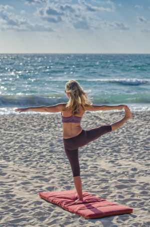 Frau am sonnigen Strand in einer Yoga-Pose. Yoga und andere Entspannungstechniken helfen Migräneattacken zu reduzieren.
